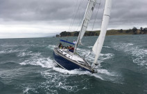 A Royal New Zealand Navy Sailing Training Craft sailing on the harbour on a grey cloudy day.