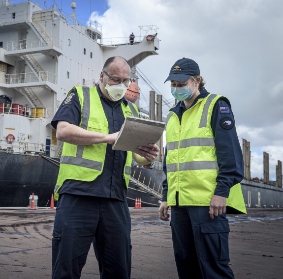 NZDF personnel working with NZ Customs personnel with a ship in the background