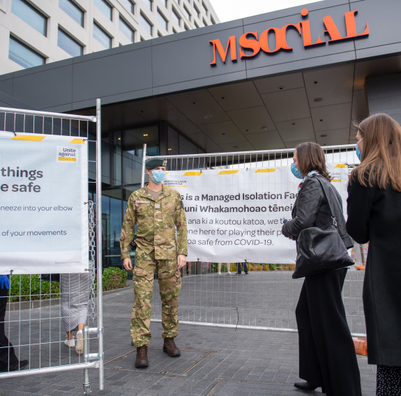 A New Zealand Army soldier at the gate of one of the COVID-19 Managed Isolation Facilities. Two people meet the soldier at the gate.