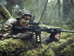 A New Zealand Army soldier in the New Zealand bush with MARS-L weapon. The area is all wet and very green. The soldier has his mouth open as he yells a command. 