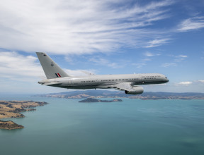 A Royal New Zealand Air Force Boeing 757-2K2 aircraft flies over the ocean but in the frame you can also see parts of land.