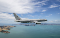 A Royal New Zealand Air Force Boeing 757-2K2 aircraft flies over the ocean but in the frame you can also see parts of land.