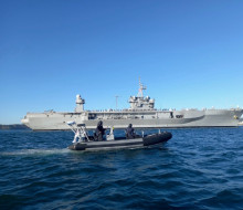 A small Royal New Zealand Navy Rigid Hull Inflatable Boat in front of the large grey US Navy ship, USS Blue Ridge.