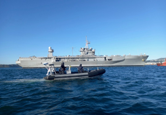 A small Royal New Zealand Navy Rigid Hull Inflatable Boat in front of the large grey US Navy ship, USS Blue Ridge.