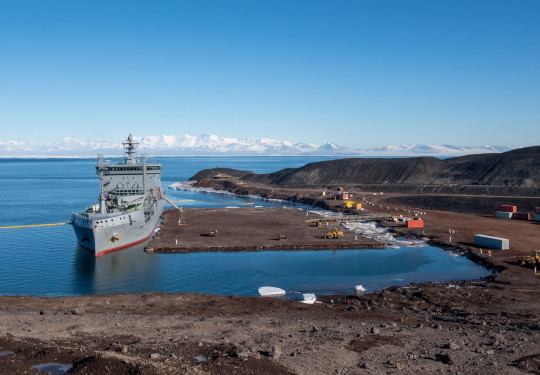 HMNZS Aotearoa and crew have berthed at Antarctica, delivering supplies and providing key support. It's a sunny day, blue sky. 