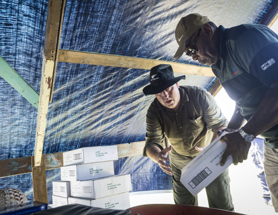 New Zealand Ministry of Foreign Affairs Liaison Officer Mr Nigel Ewels (left) helps stack food aid supplies on Yacata Island after delivery by the Seasprite helicopter.