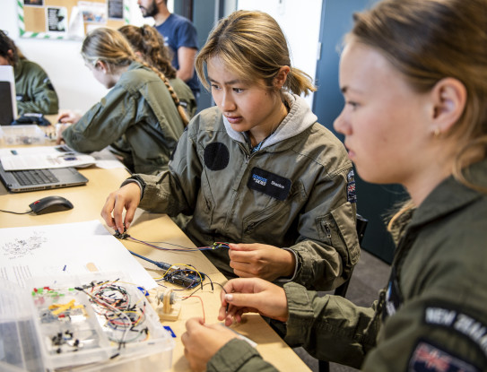 Two School to Skies participants work in flight suits work together to assemble small parts