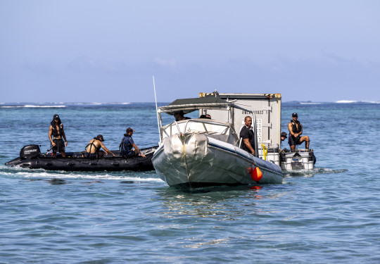 Two rigid hull inflatable boats manoeuver a shipping container at sea. The container has been floated using rigid pontoons.