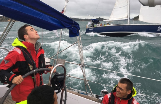 Navy trainees wearing red jackets and life jackets sailing through choppy waves 