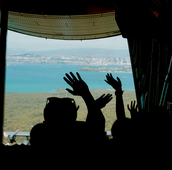 Children silhouetted by the open read door of the C-130H Hercules wave as they fly away from Auckland City.