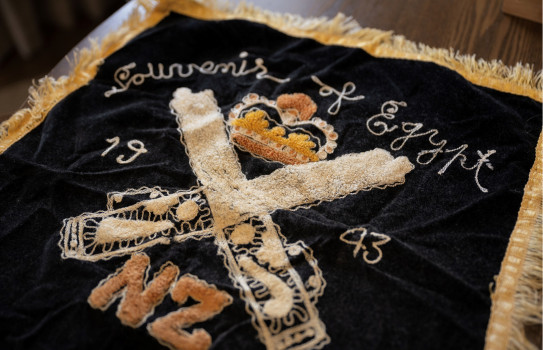 Photo of an embroidered flag from 1943, featuring the letters 'NZ", and crown and the year it was made.