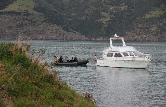 Navy sailors in a RHIB talk to a civilian sailor on their own vessel.