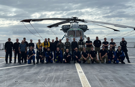 Group photo of sailors and aviators. In front of a Seasprite helicopter on the flight deck, they are in two ranks, some kneeling and others standing.