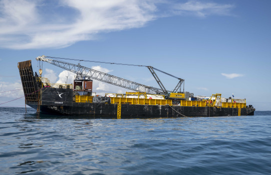 A black and yellow barge at sea. A large crane is embarked on the barge. No land is in sight.